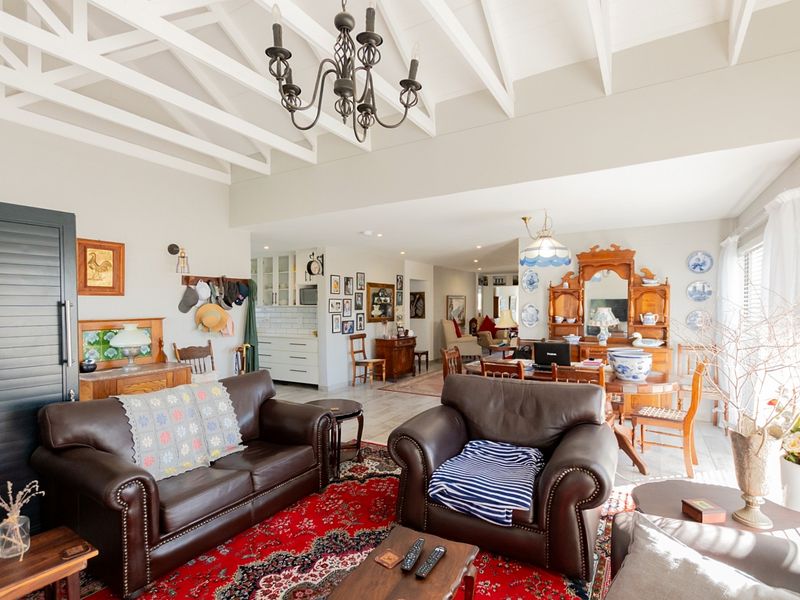 Spacious open-plan living and dining area featuring high vaulted ceilings with exposed beams, a classic chandelier, and a seamless transition to the kitchen.