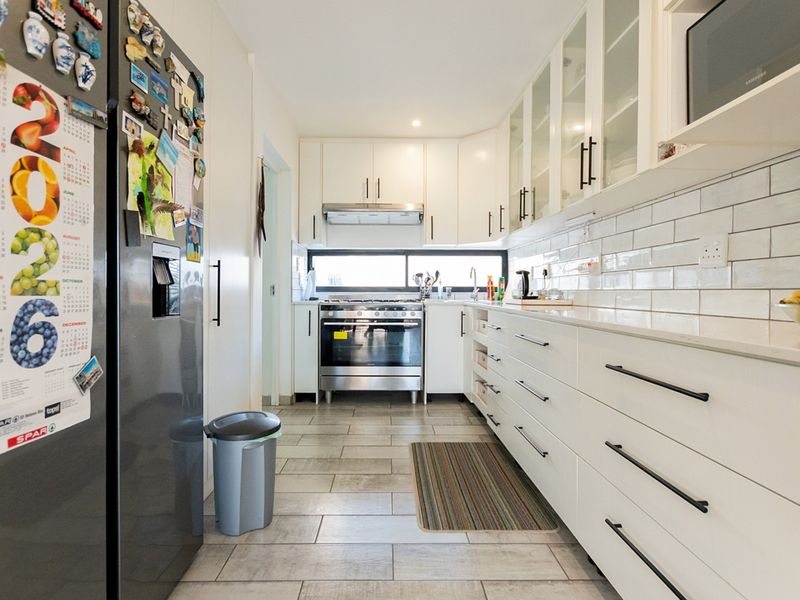 Modern galley-style kitchen featuring white cabinetry, stone countertops, subway tile backsplash, and stainless steel appliances, offering a clean and functional cooking space.