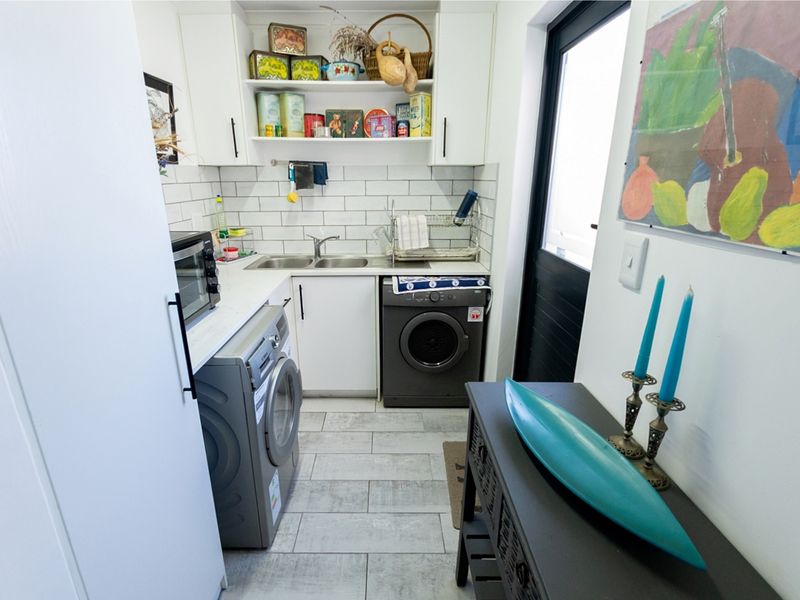 Compact laundry area featuring subway tile backsplash, built-in cabinetry, stainless steel double sink, and direct access to the exterior.
