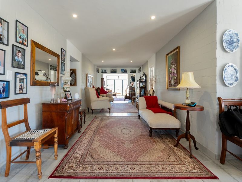 A spacious, light-filled hallway featuring painted brick walls, recessed downlighting, and neutral tiled flooring, leading through to the main living areas.