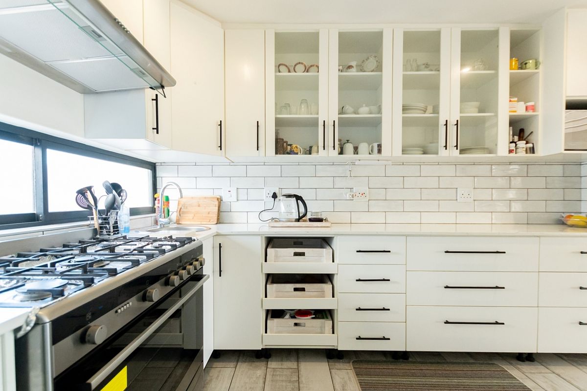 A well-maintained kitchen featuring white cabinetry, subway tile backsplash, quartz countertops, and a stainless steel gas stove with an integrated extractor fan.