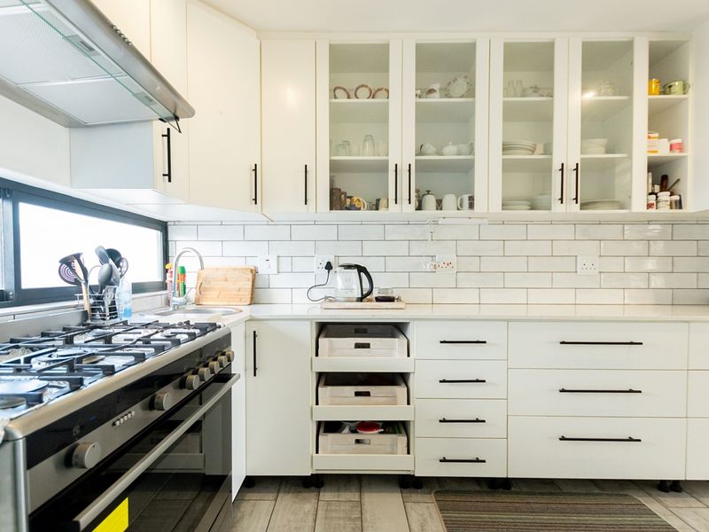 A well-maintained kitchen featuring white cabinetry, subway tile backsplash, quartz countertops, and a stainless steel gas stove with an integrated extractor fan.