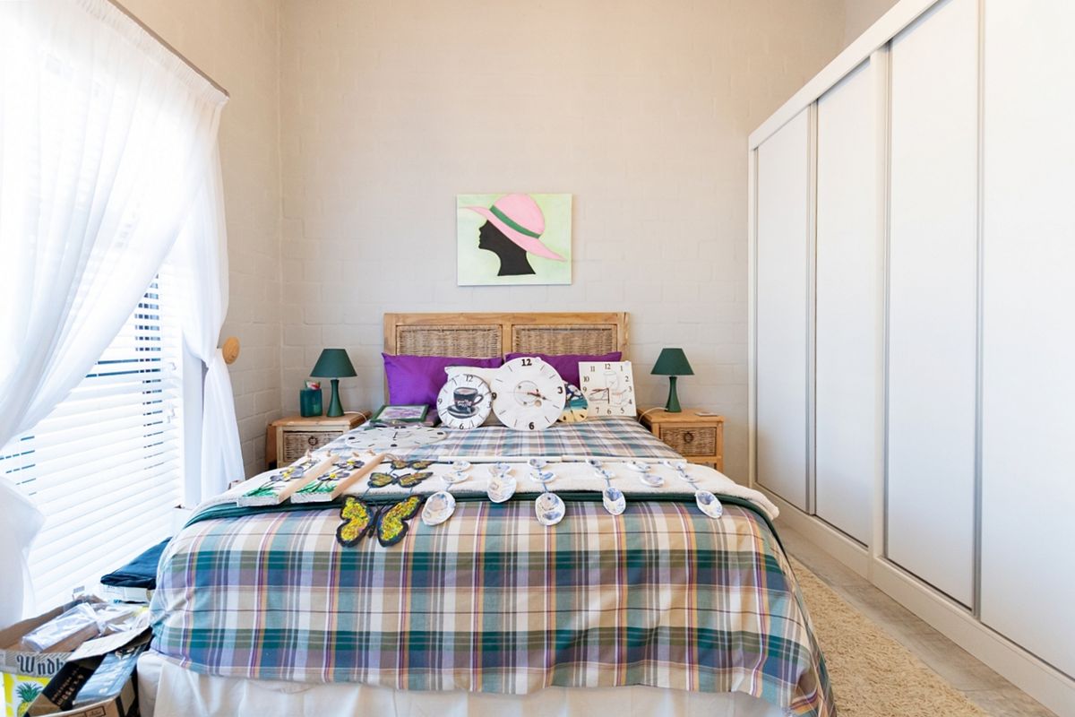 A well-maintained bedroom featuring neutral painted brick walls, tiled flooring, and a large built-in wardrobe with sliding doors.
