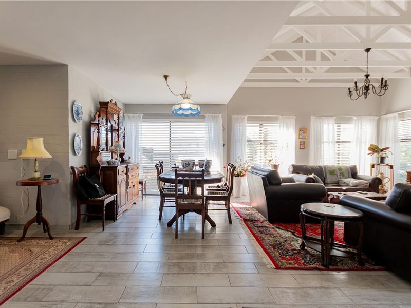 Spacious open-plan living and dining area featuring high vaulted ceilings with exposed timber trusses, tiled flooring, and abundant natural light through large windows.