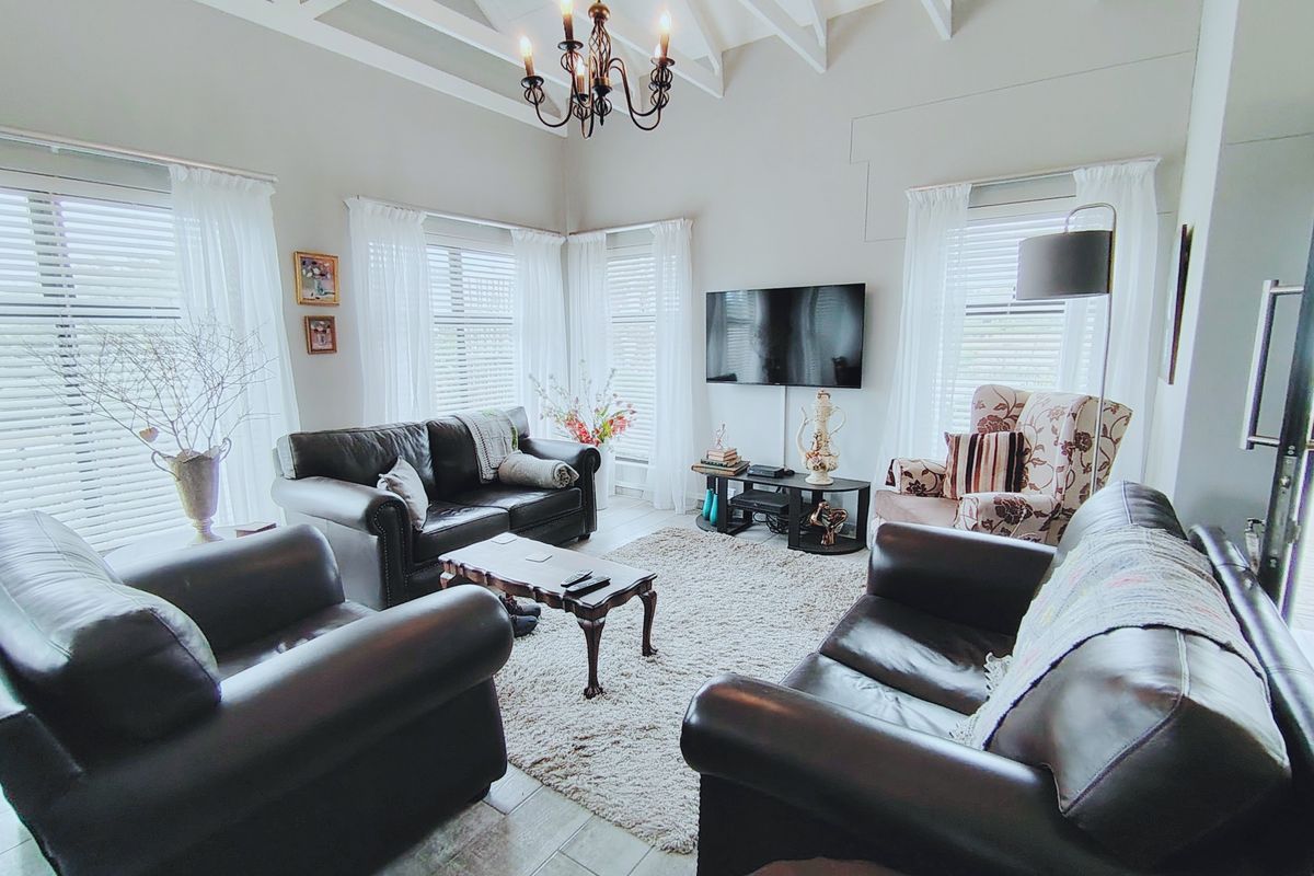 Spacious living room featuring high vaulted ceilings with exposed rafters, tiled flooring, and abundant natural light through multiple windows with venetian blinds.