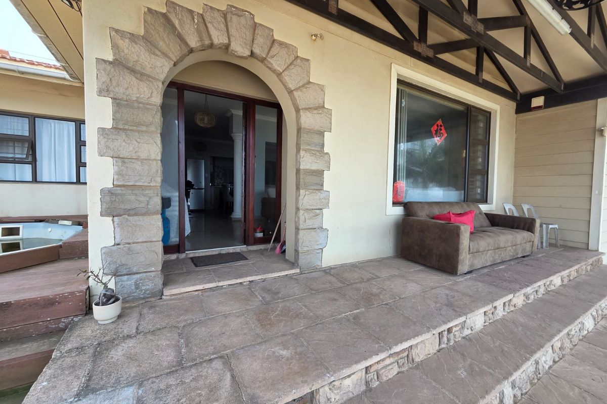 A covered patio area featuring stone flooring, a decorative stone archway entrance, exposed timber roof trusses, and an integrated spa pool.