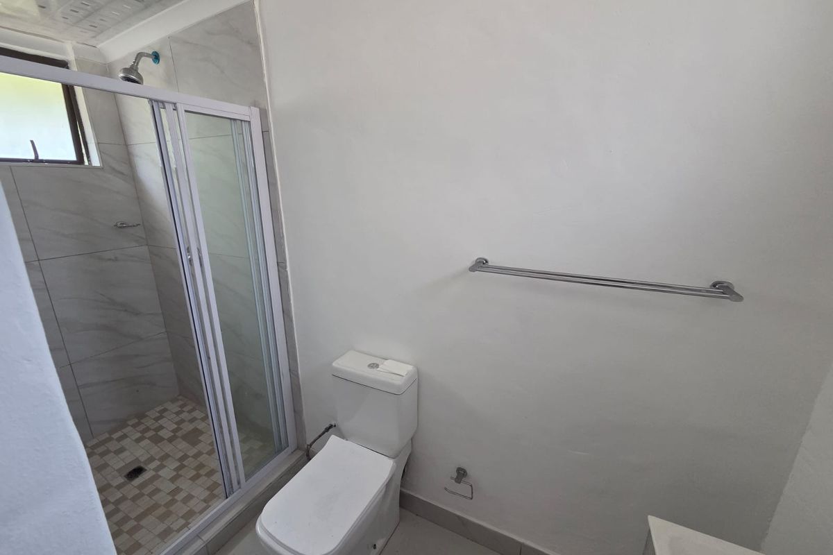 A functional bathroom featuring a glass-enclosed shower, a modern toilet, and a wall-mounted towel rail with neutral tiled finishes.