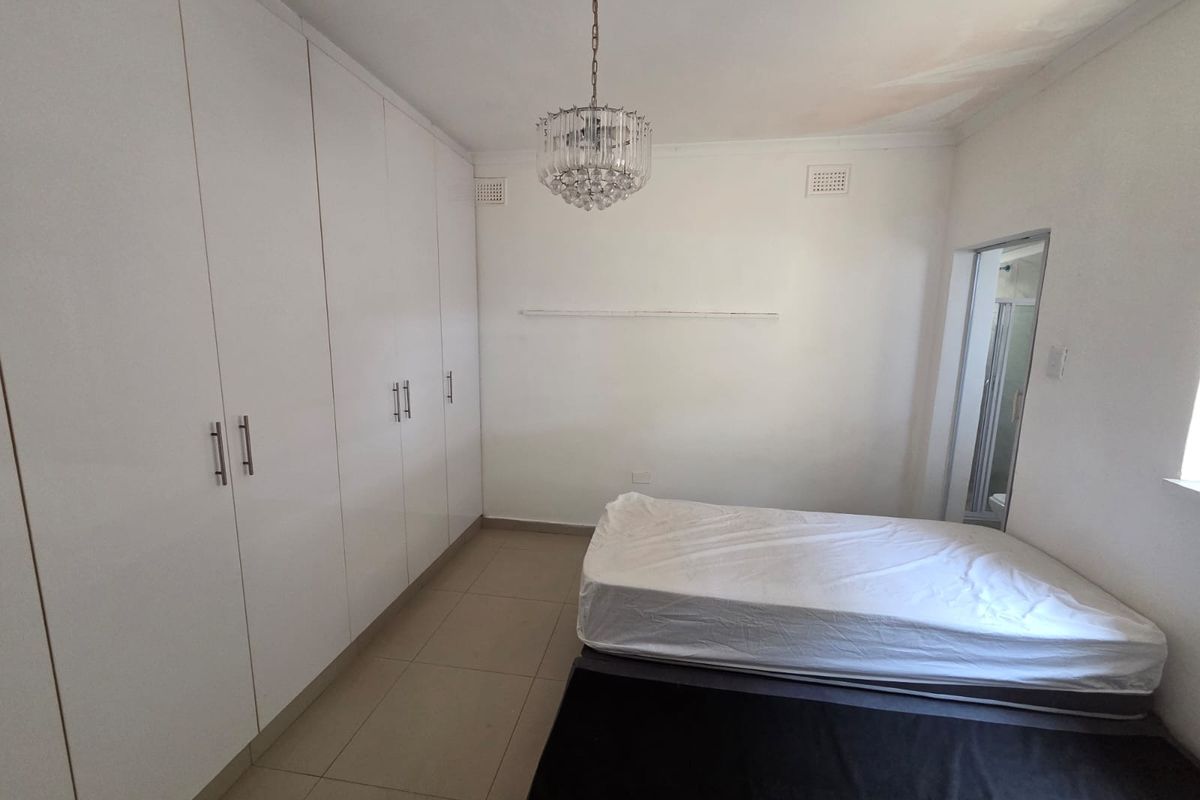 A bedroom featuring extensive built-in cupboards, tiled flooring, and an en-suite bathroom, with visible ceiling staining requiring attention.