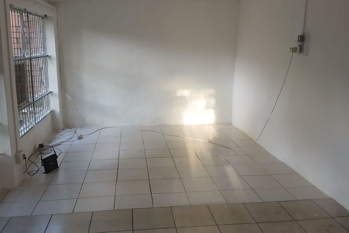 An empty living room featuring tiled flooring and security bars on the windows, requiring minor cosmetic updates and electrical tidying.