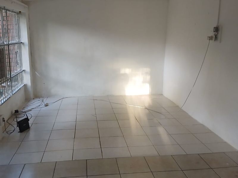 An empty living room featuring tiled flooring and security bars on the windows, requiring minor cosmetic updates and electrical tidying.