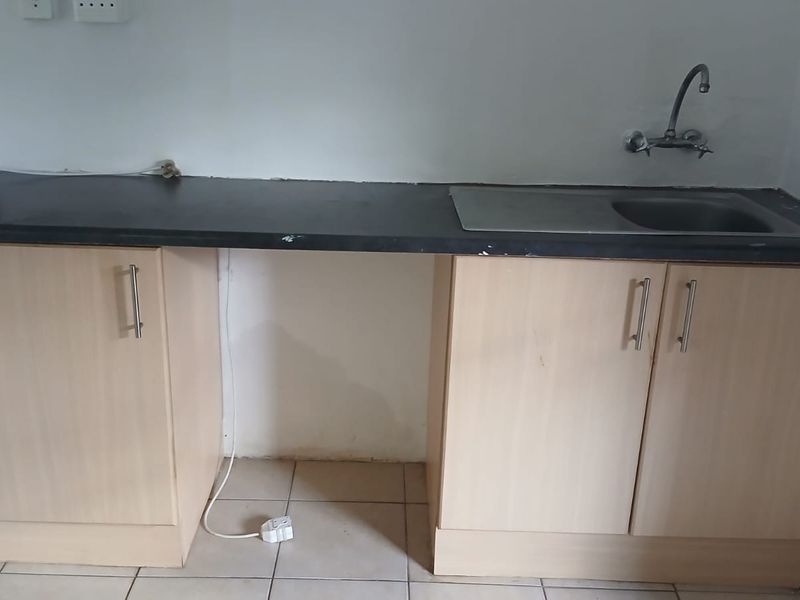 A basic kitchen kitchenette area featuring light wood-look cabinetry, a dark laminate countertop, and a single stainless steel sink.