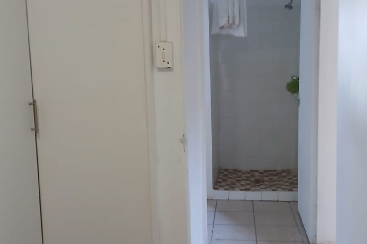 A functional bathroom area featuring a built-in cupboard and a shower enclosure with tiled flooring.