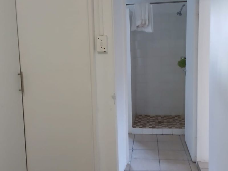 A functional bathroom area featuring a built-in cupboard and a shower enclosure with tiled flooring.