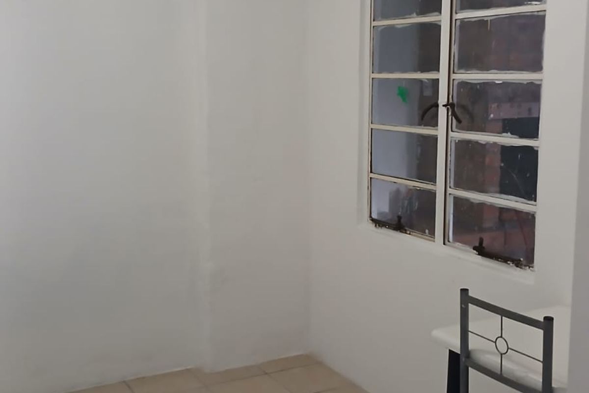 A simple, empty bedroom featuring tiled flooring, a multi-pane window, and a ceiling-mounted spotlight fixture, ready for personalization.