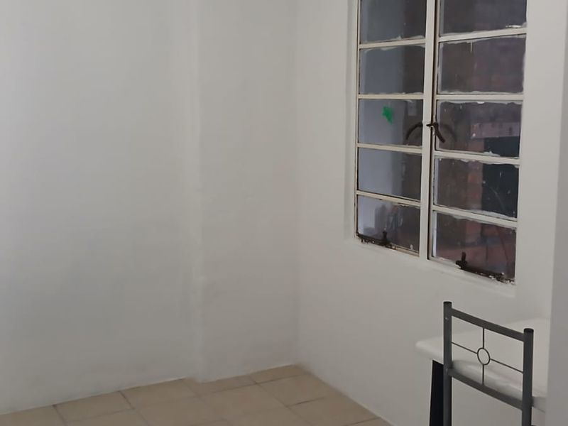 A simple, empty bedroom featuring tiled flooring, a multi-pane window, and a ceiling-mounted spotlight fixture, ready for personalization.