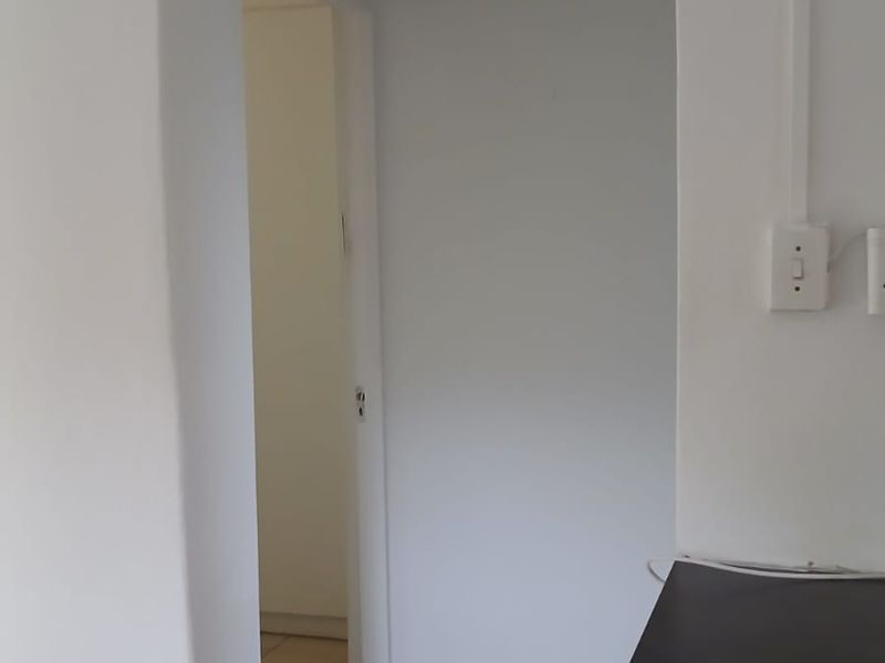 A simple interior hallway with tiled flooring and white walls, connecting to an adjacent room.
