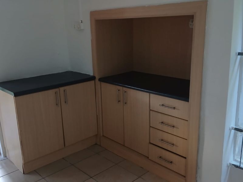 A functional scullery or utility area featuring built-in light wood cabinetry, dark laminate countertops, and tiled flooring with direct access to the exterior.