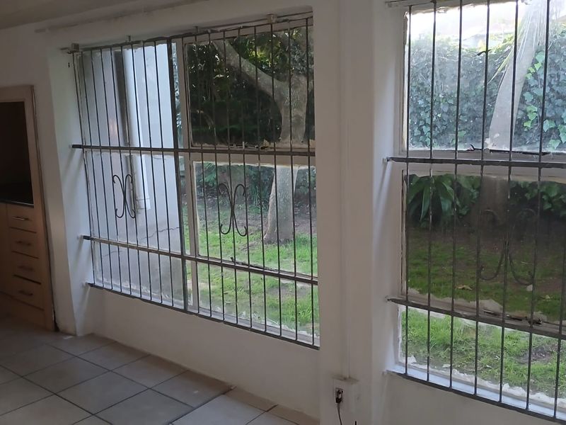 An empty kitchen area featuring tiled flooring, built-in cabinetry, and large windows with security bars overlooking the garden.