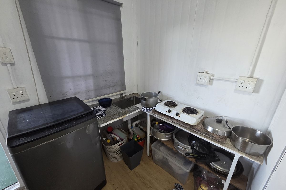 A compact, basic kitchenette area featuring a small sink, countertop space, and exposed electrical fixtures, requiring significant modernization and finish improvements.