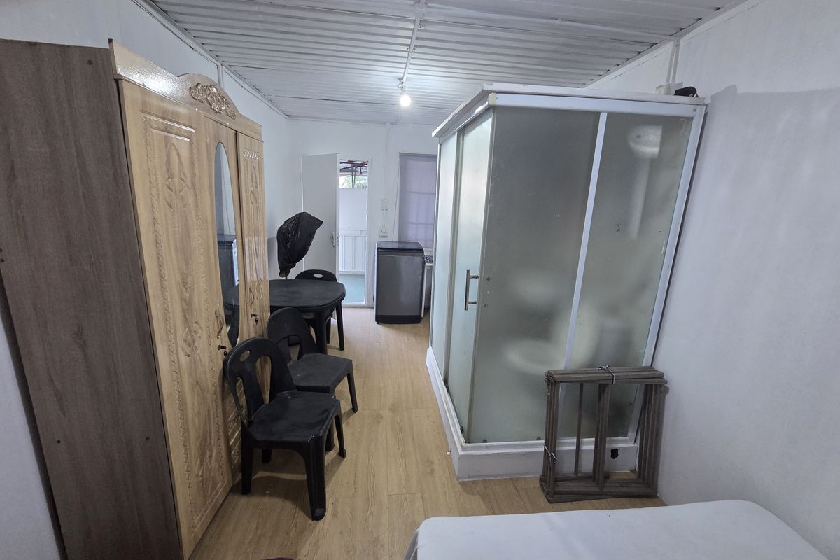 A bedroom featuring laminate flooring and an integrated shower cubicle, with a basic corrugated metal ceiling finish.