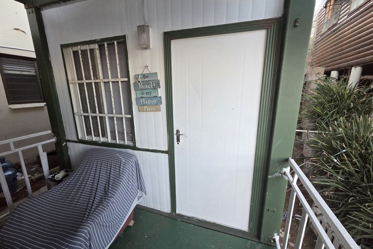 A covered balcony area featuring security bars on the window, metal railings, and weathered exterior finishes, providing a functional outdoor space.