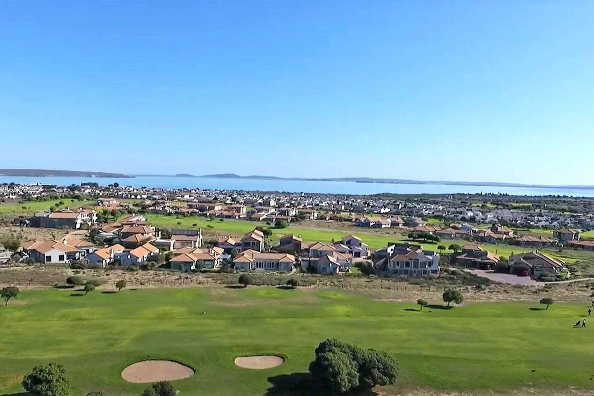An aerial view showcasing the property's location overlooking a golf course with expansive coastal and residential views in the background.