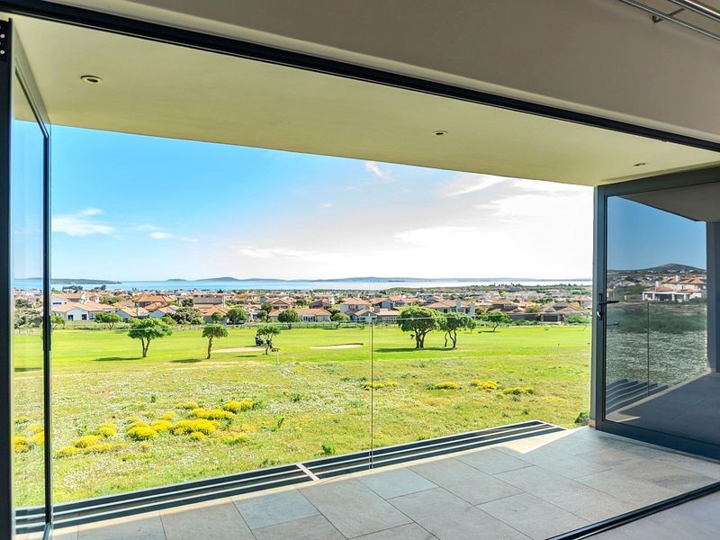 A modern covered balcony featuring tiled flooring, a sleek glass balustrade, and expansive folding doors offering panoramic views of the golf course and ocean.