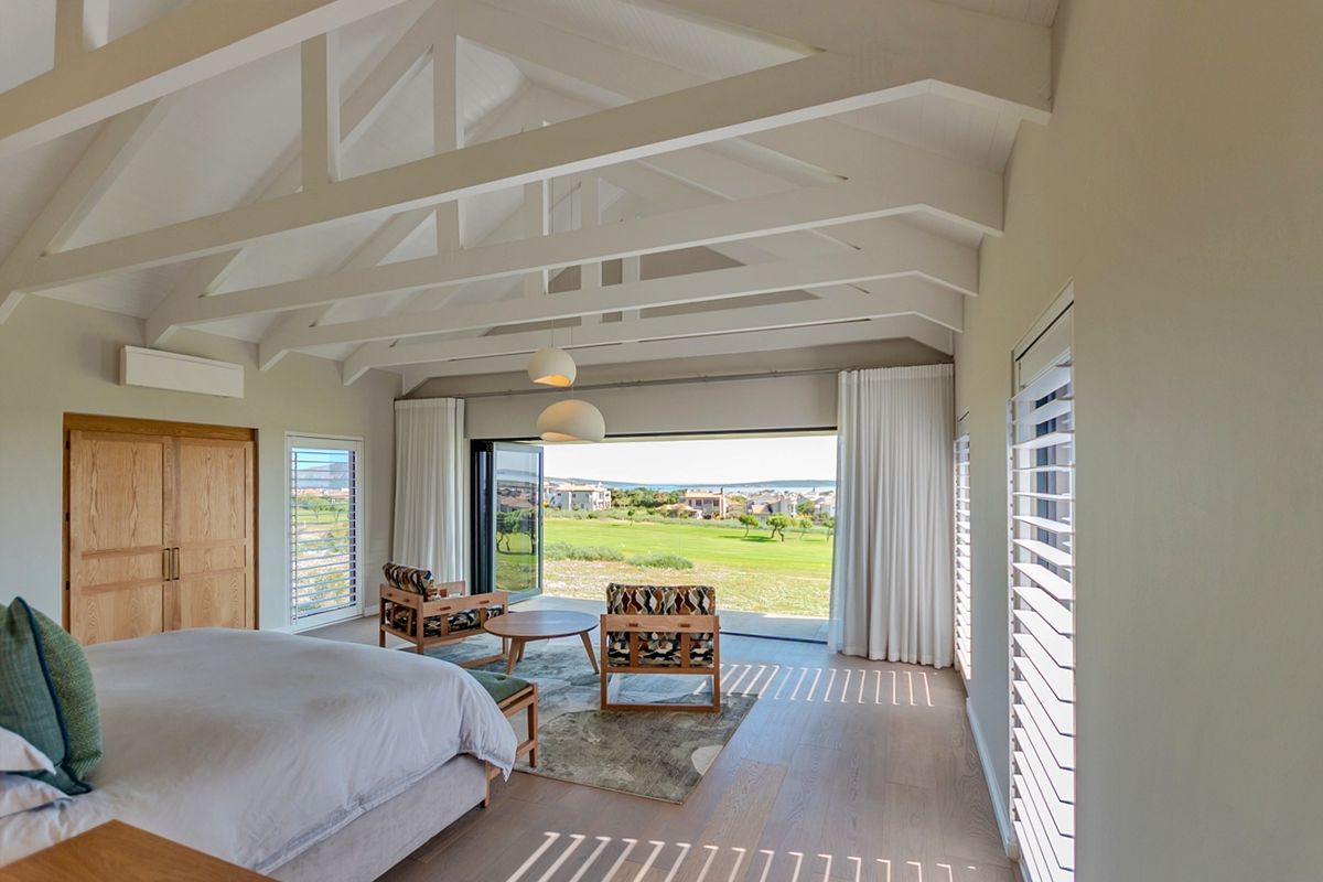 Spacious bedroom featuring a vaulted ceiling with exposed trusses, timber flooring, built-in cabinetry, and large stacking doors opening to a scenic golf course view.