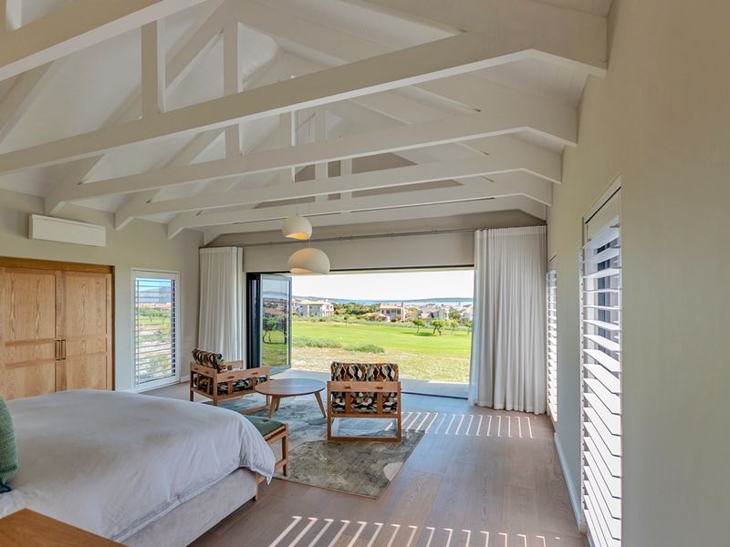 Spacious bedroom featuring a vaulted ceiling with exposed trusses, timber flooring, built-in cabinetry, and large stacking doors opening to a scenic golf course view.