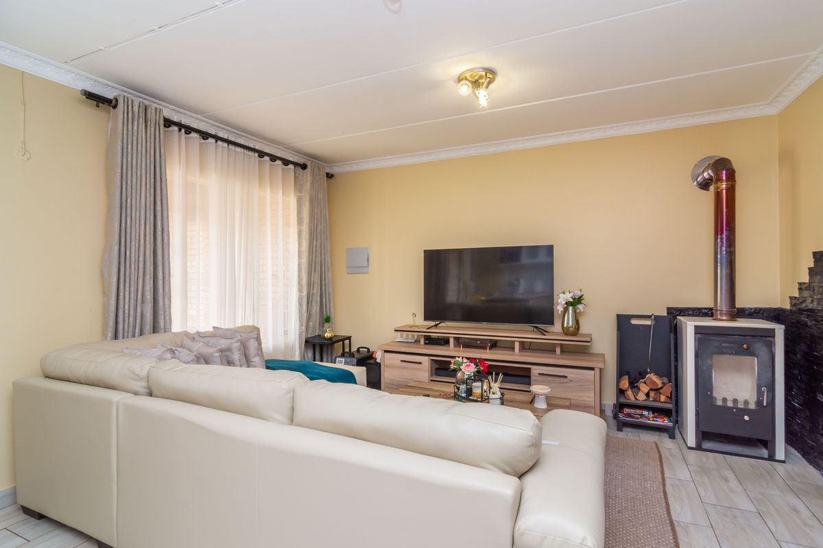 A comfortable living room featuring tiled flooring, a built-in fireplace with a flue, and large windows with curtain rails.