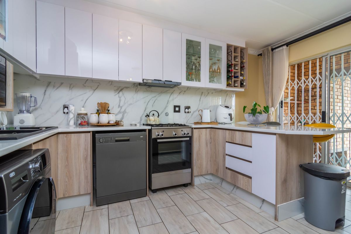 Modern kitchen featuring white gloss and wood-grain cabinetry, marble-look splashback, gas hob, oven, and tiled flooring with direct access to the patio.