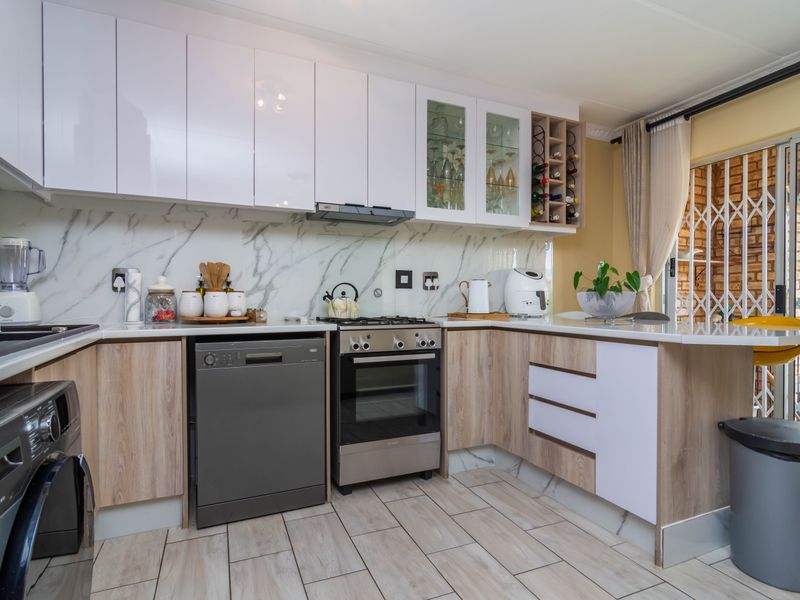 Modern kitchen featuring white gloss and wood-grain cabinetry, marble-look splashback, gas hob, oven, and tiled flooring with direct access to the patio.