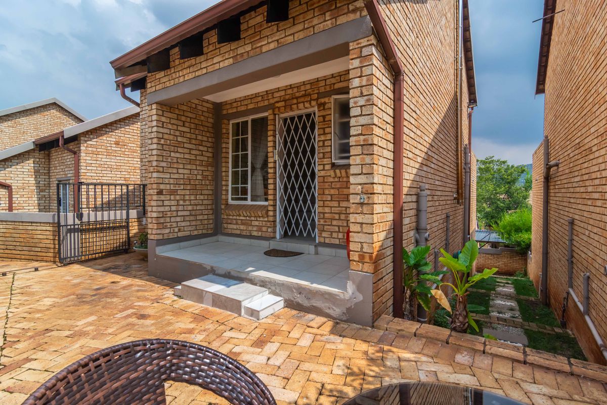 Rear view of a face brick townhouse featuring a paved courtyard and a covered patio entrance with a security gate.