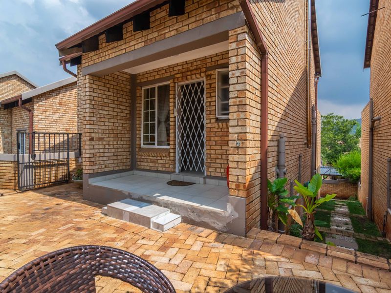 Rear view of a face brick townhouse featuring a paved courtyard and a covered patio entrance with a security gate.