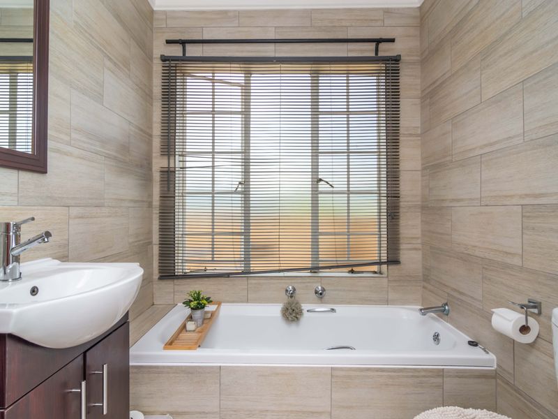 A modern bathroom featuring a built-in bathtub, vanity with basin, and neutral wall tiling, creating a clean and functional space.