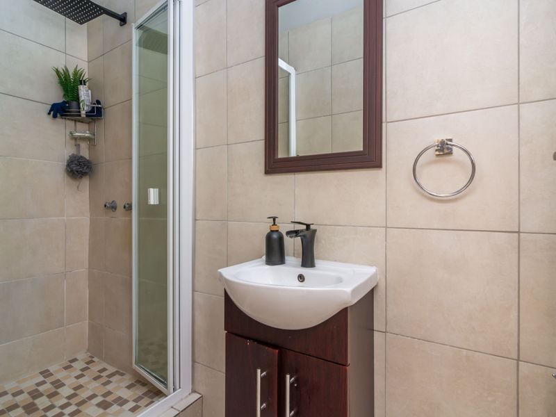 A modern bathroom featuring a glass-enclosed shower with a rain shower head, a vanity cabinet with a basin, and neutral wall tiling.