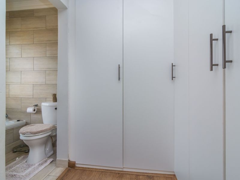 A clean bathroom featuring built-in storage cupboards, a standard toilet, and a bathtub with neutral wall tiling.