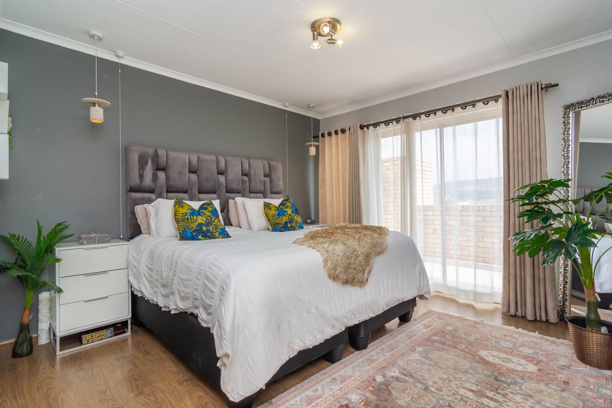 A well-maintained bedroom featuring laminate flooring, modern pendant lighting, and a large sliding glass door providing access to an outdoor balcony area.