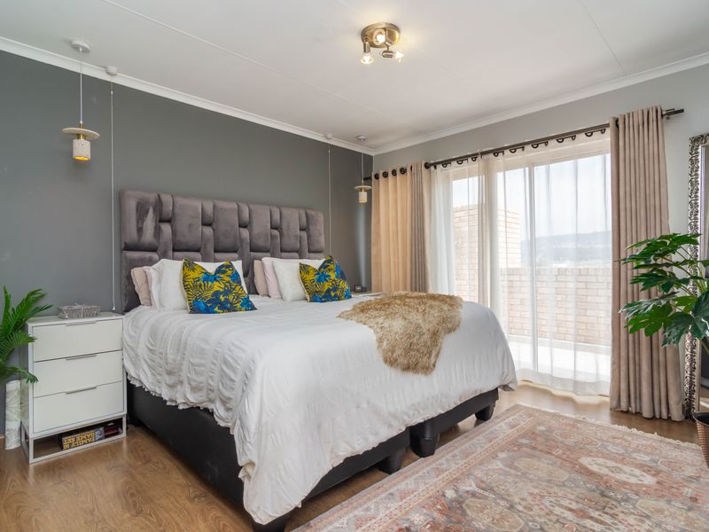 A well-maintained bedroom featuring laminate flooring, modern pendant lighting, and a large sliding glass door providing access to an outdoor balcony area.