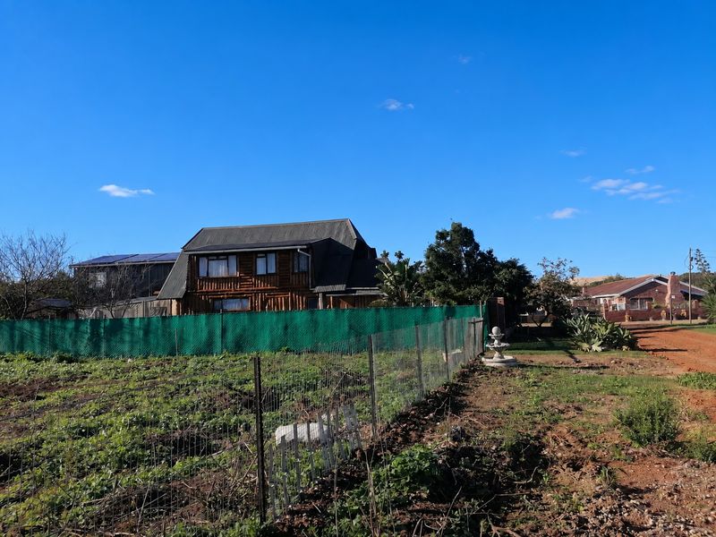 View of a residential property featuring a log cabin style home, wire fencing, and a garden fountain on a dirt road.