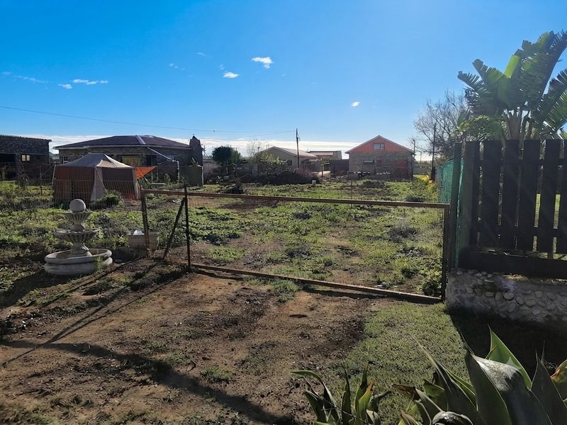 A view of a vacant residential plot featuring a metal gate entrance, perimeter fencing, and natural ground cover.