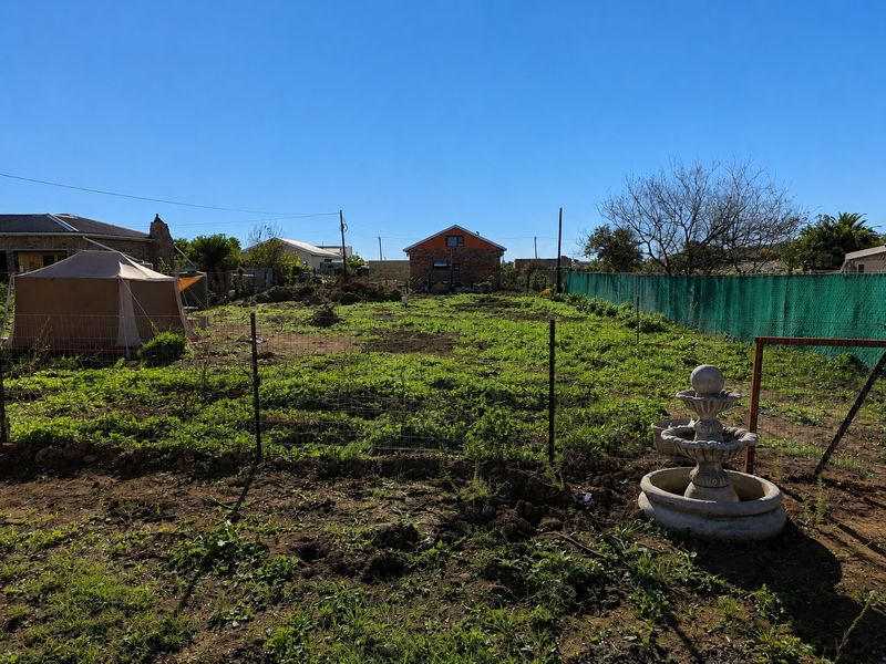 A vacant residential plot featuring a stone fountain, wire perimeter fencing, and natural vegetation, offering potential for landscaping or future development.