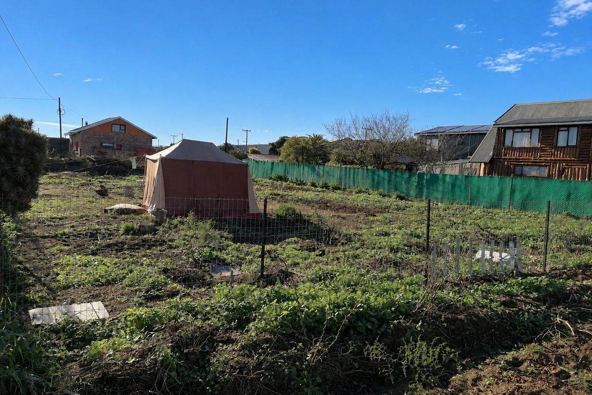 A vacant residential plot featuring wire mesh fencing and green perimeter screening, offering a blank canvas for future development.