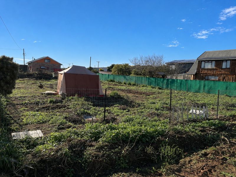 A vacant residential plot featuring wire mesh fencing and green perimeter screening, offering a blank canvas for future development.
