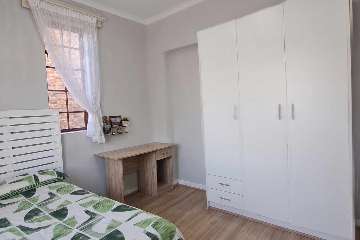A well-maintained bedroom featuring light-toned laminate flooring, neutral wall finishes, and a large white built-in wardrobe providing ample storage space.