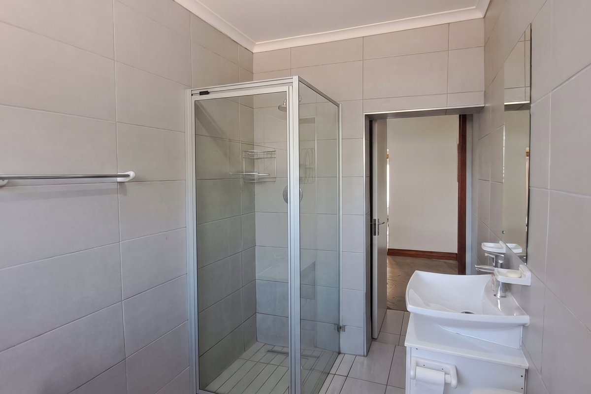 A clean, modern bathroom featuring a glass shower enclosure, wall-mounted basin, and neutral floor-to-ceiling wall tiles.