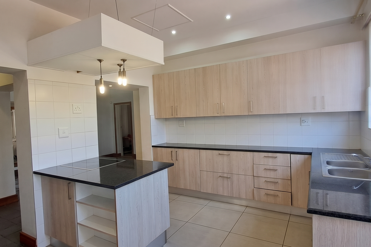 Modern kitchen featuring light wood-finish cabinetry, granite countertops, a built-in hob, and a double stainless steel sink with tiled splashbacks.