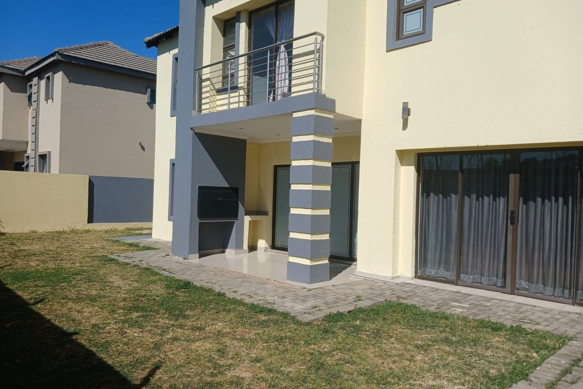Rear view of the townhouse featuring a paved patio area with a built-in braai, a balcony above, and access via sliding glass doors.