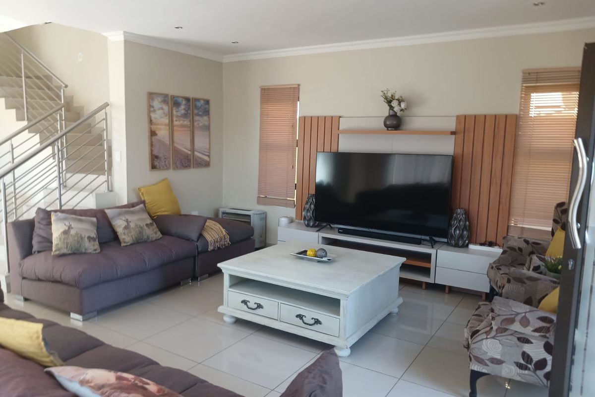 Spacious living room featuring tiled flooring, a modern staircase with stainless steel balustrades, and a built-in media wall unit.