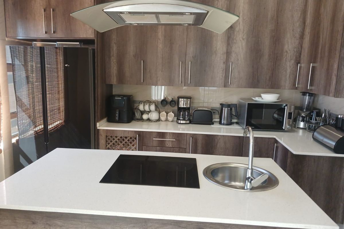 Modern kitchen featuring wood-grain cabinetry, stone countertops, a central island with an integrated hob and sink, and a stainless steel extractor fan.